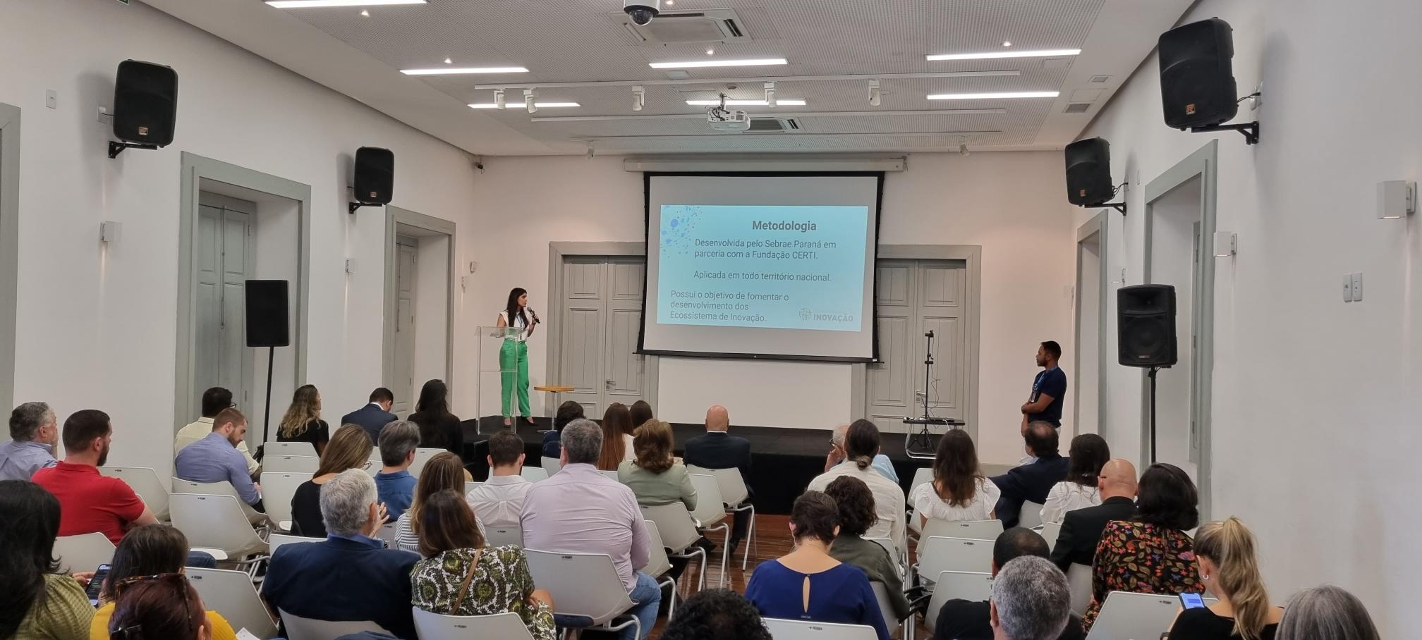 Diversas pessoas sentadas olhando para um uqadro branco onde está projetada uma apresentação sobre melhorias para o Centro do Rio.