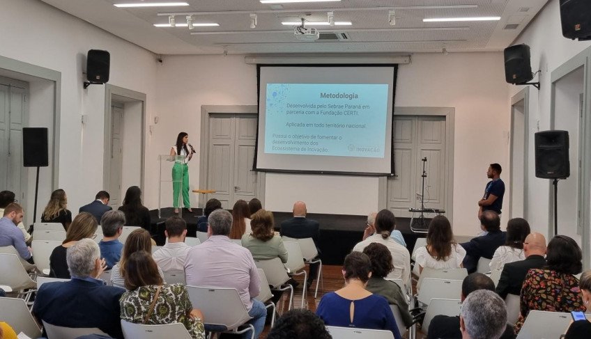 Diversas pessoas sentadas olhando para um uqadro branco onde está projetada uma apresentação sobre melhorias para o Centro do Rio.